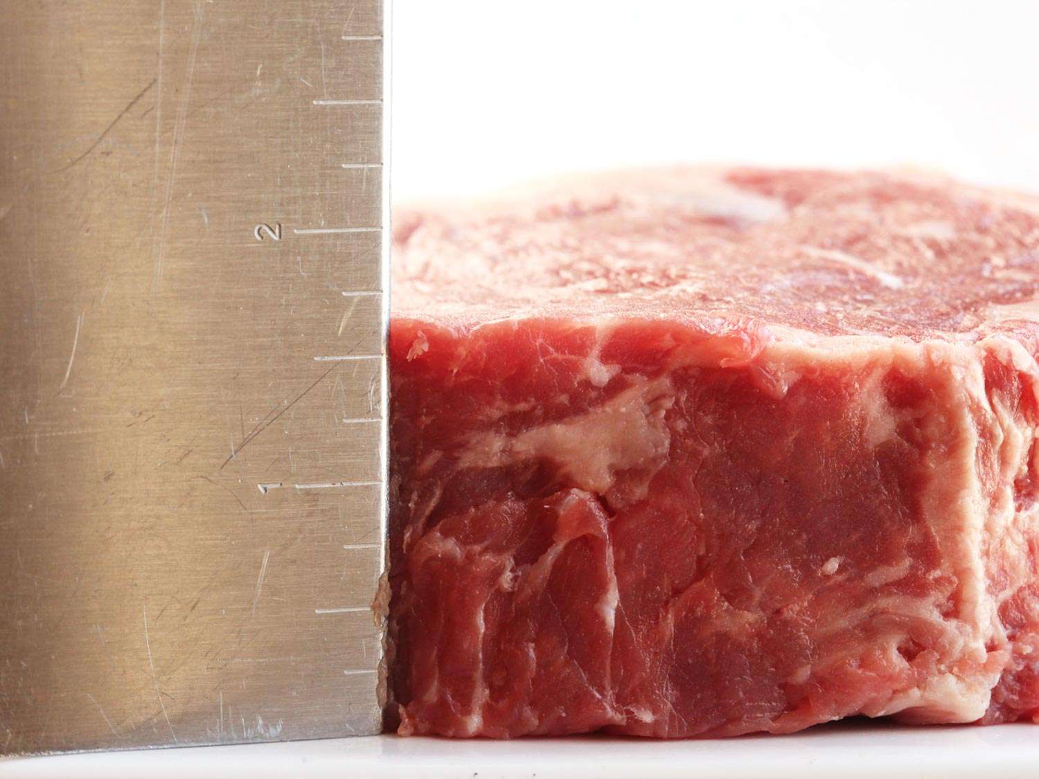 A cut of raw steak with a ruler next to it showing that it is one and a half inches thick.