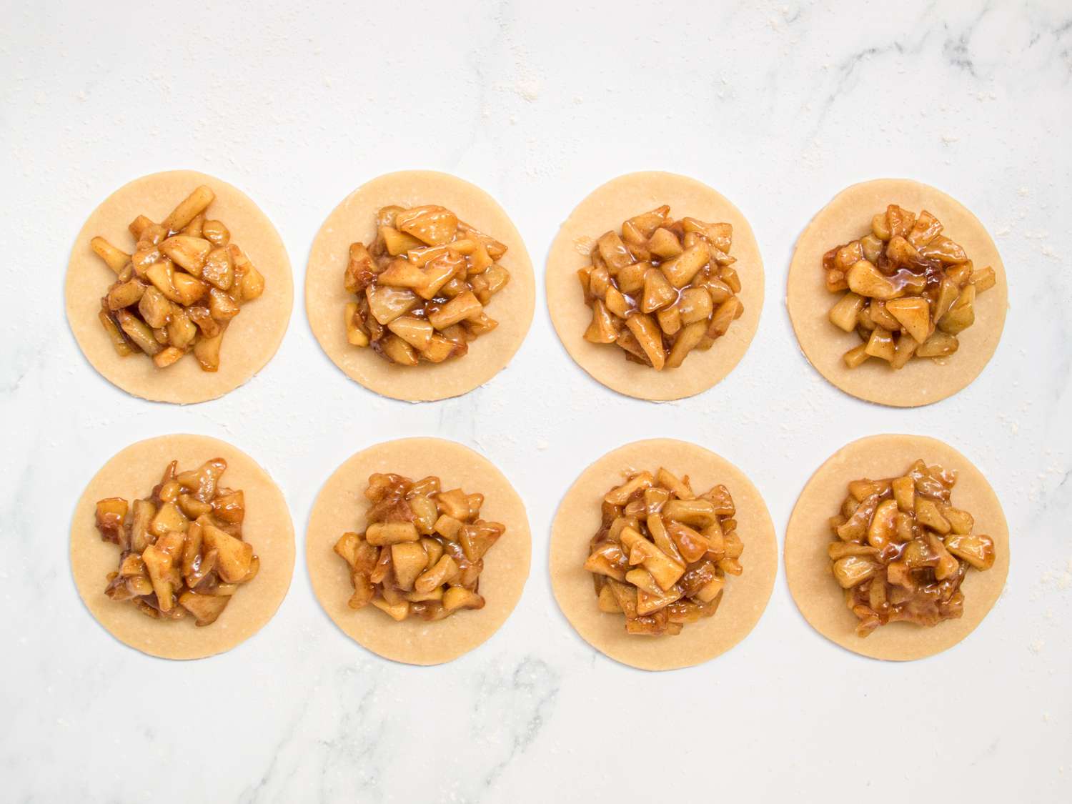 8 dough rounds on a lightly floured surface with apple mixture filling in the center of each round