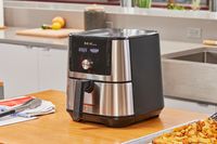 The Instant Vortex Plus 6QT XL Air Fryer on a wooden counter next to a baking sheet of fries