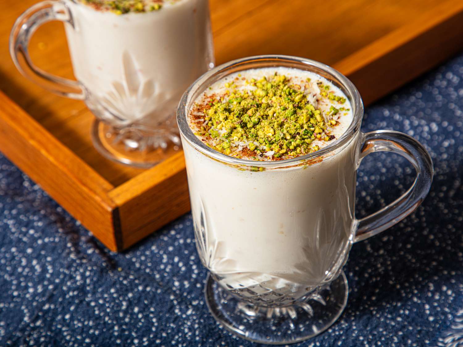 Two glasses of sahlab topped with pistachios and spices on a tray