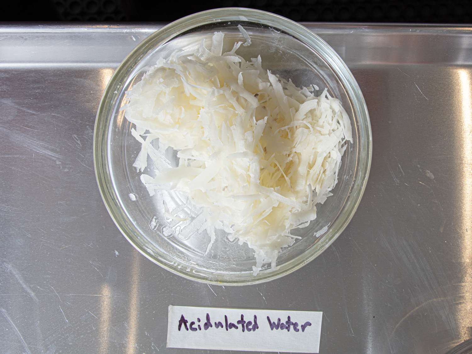 Shredded material in a glass bowl labeled Acidulated Water placed on a metallic surface