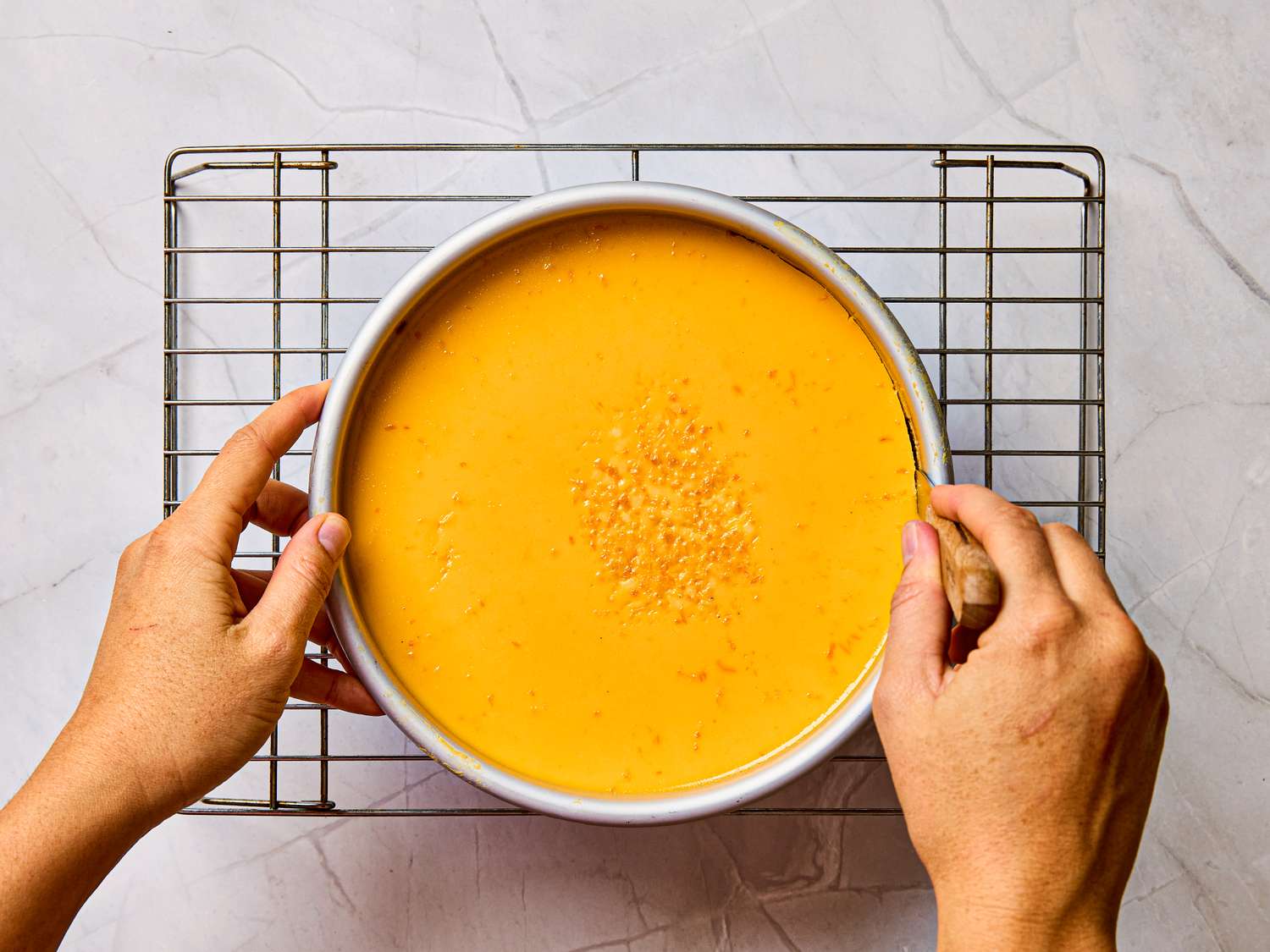 Hands holding a rack with a prepared flan dessert in a round dish
