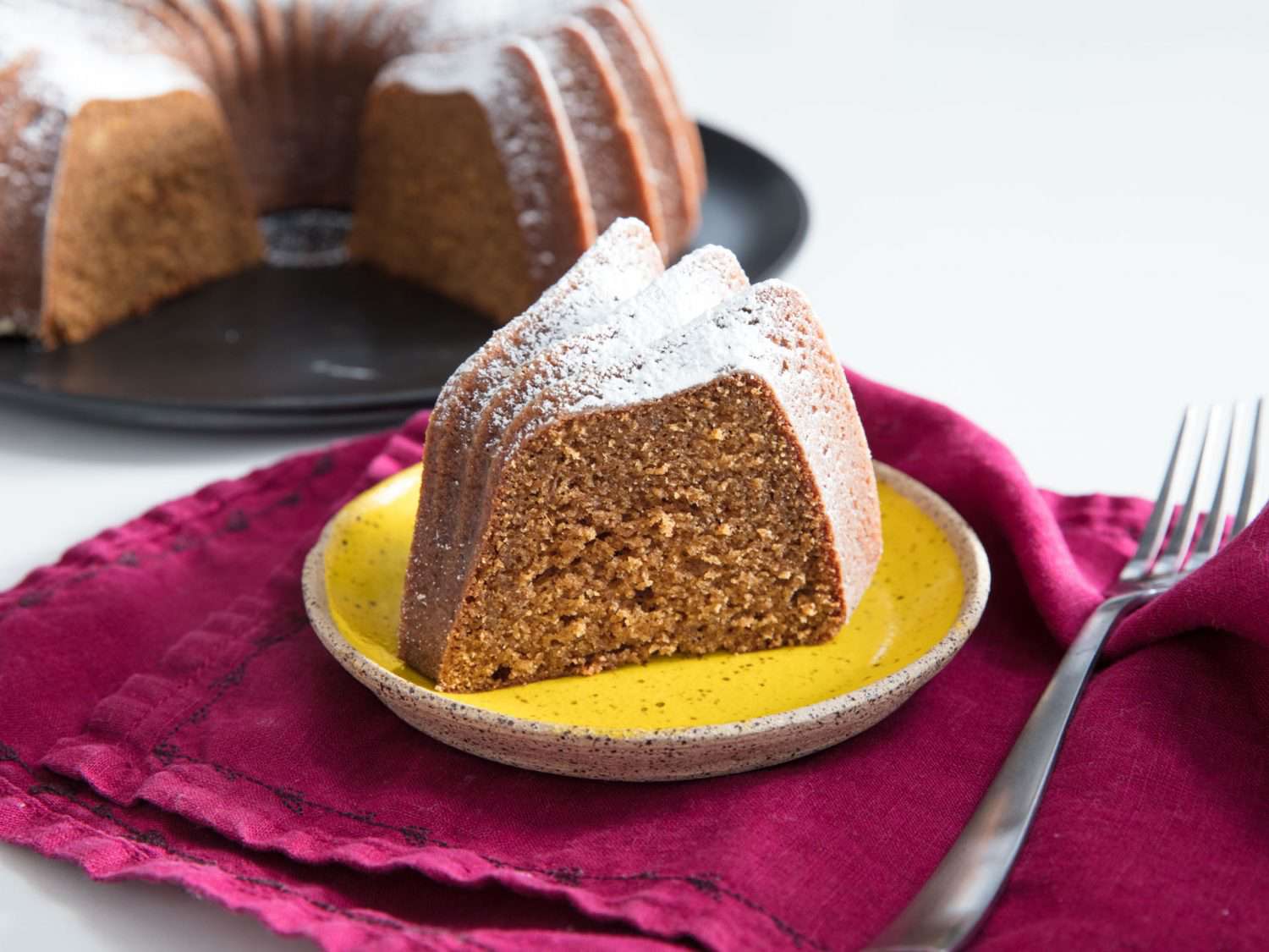 A plated slice of gingerbread bundt cake dusted with confectioners' sugar.