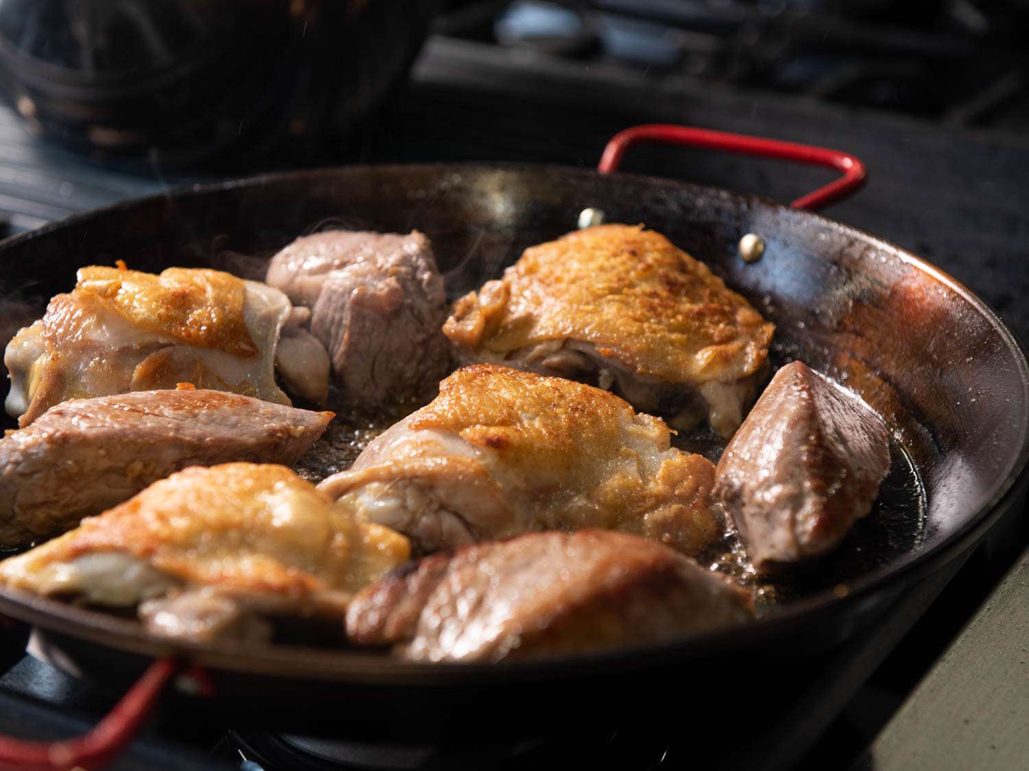 Pan-frying chicken thighs and chunks of pork for paella. 
