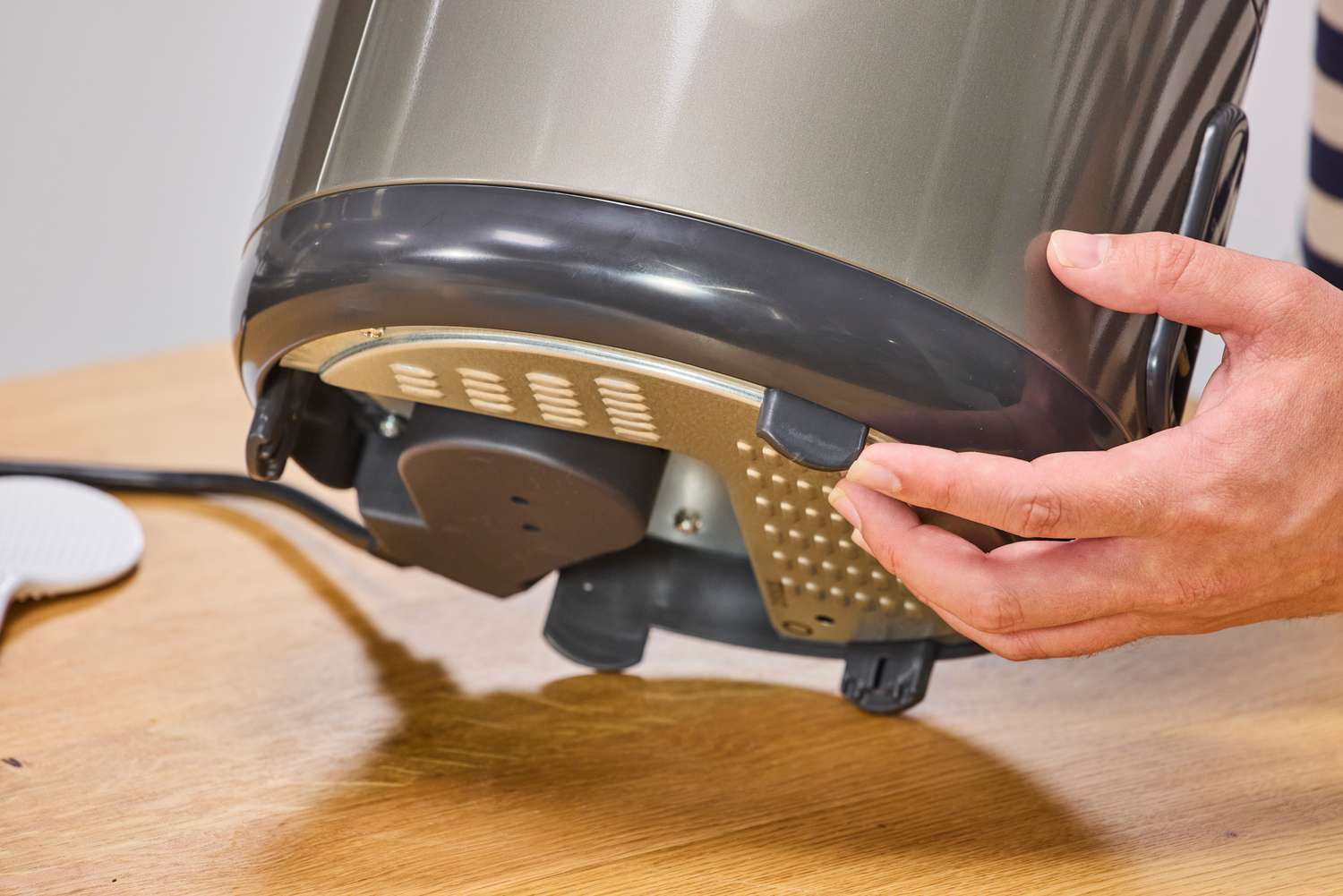 A person lifts the Zojirushi NS-RPC10HM Rice Cooker showing the feet on the bottom