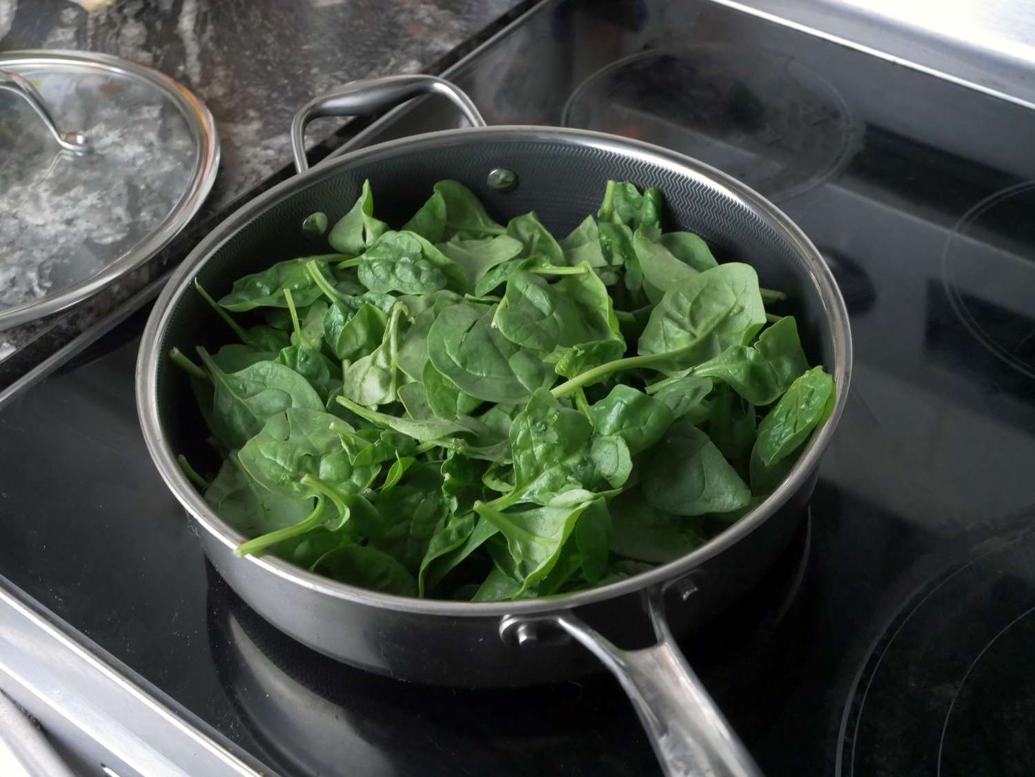 a saute pan on a glass stove with spinach inside