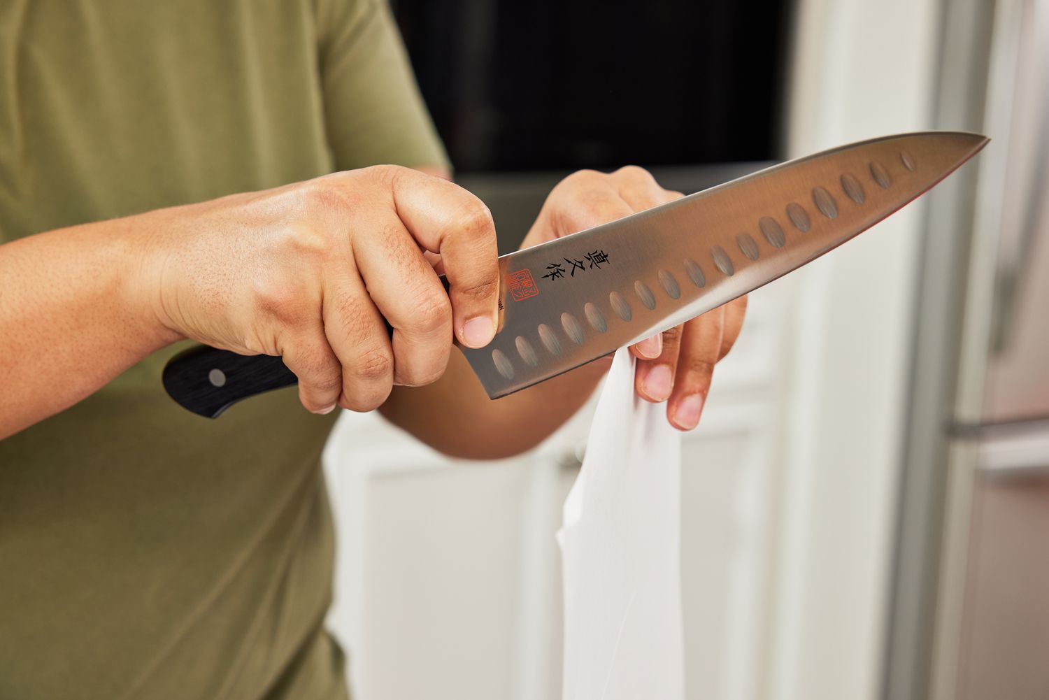 A hand holding a Japanese-style chef's knife and using it to slice through a sheet of printer paper