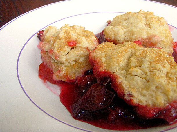 A large serving of plum and ginger cobbler plopped unto a white plate.