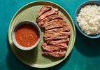 Crying Tiger (Thai-style grilled steak) on a green ceramic plate, with a small ceramic bowl holding the dry chile dipping sauce). On the periphery is a small bowl of white rice.