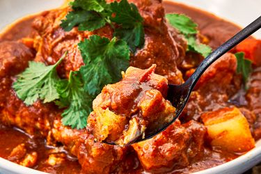 Closeup of Pollo Guisado served in a bowl with a spoon lifting a bite garnished with cilantro