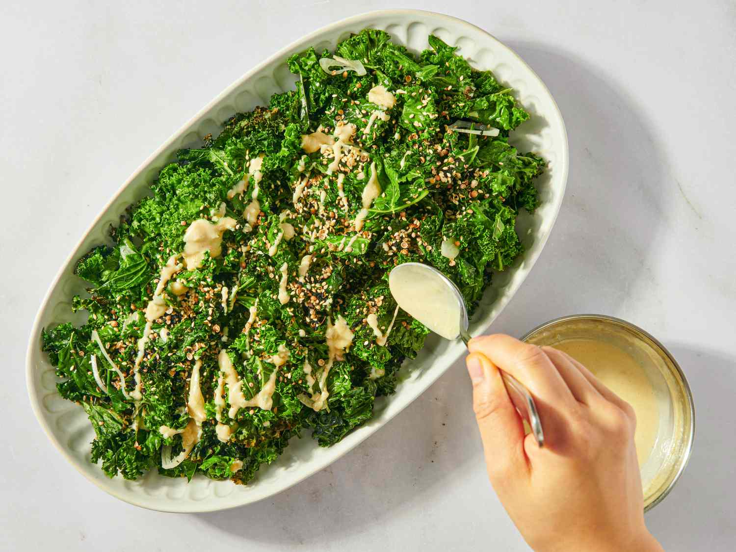 Hand drizzling dressing onto a plate of kale salad with seeds