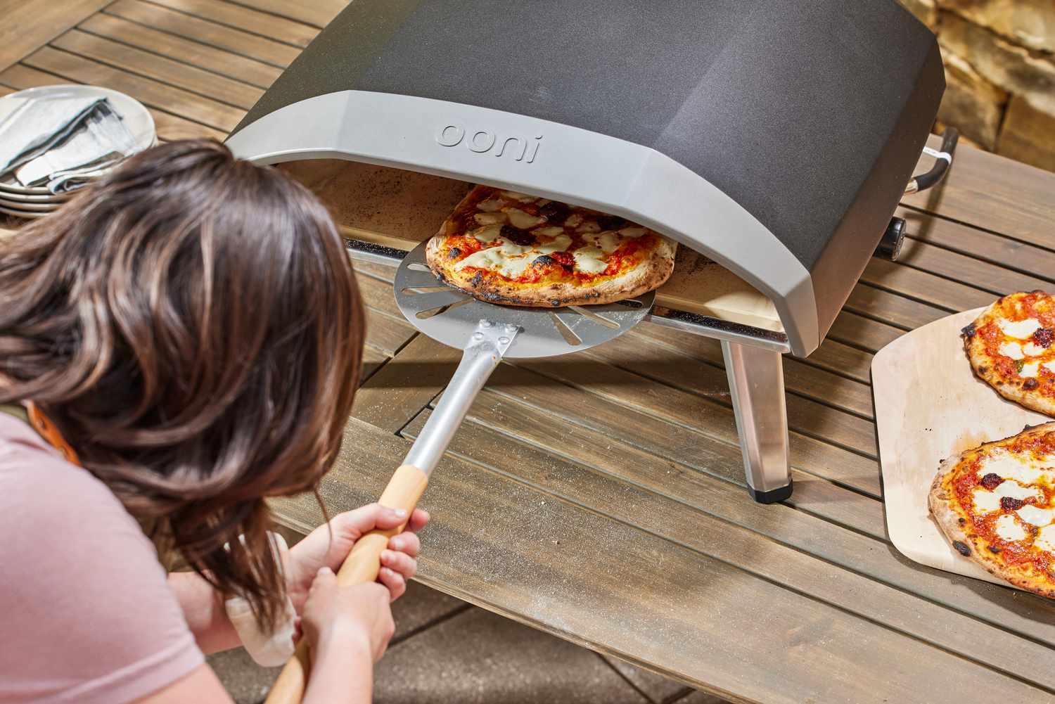 A person removing a pie from the Ooni Koda 16 Gas Pizza Oven