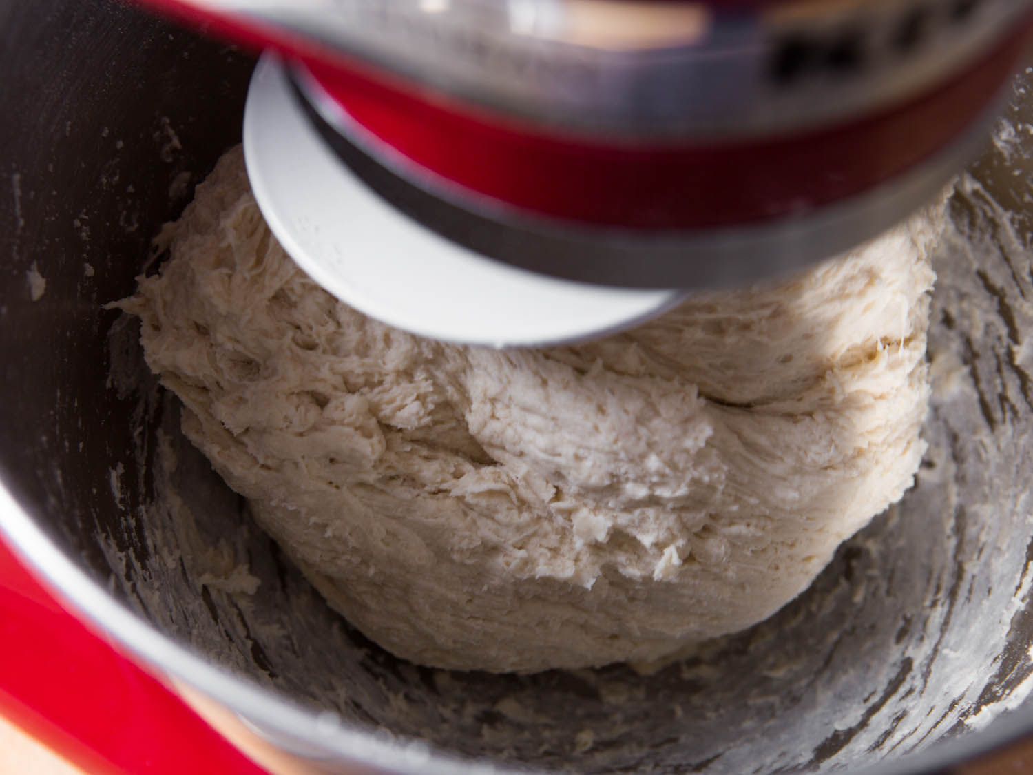 Yeast, flour, and water being mixed together in a red stand mixer.