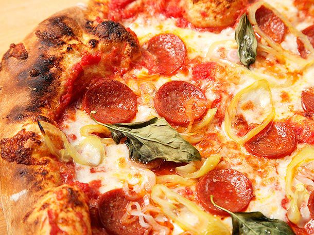 Closeup of pepperoni pizza topped with pickled banana peppers and basil leaves.