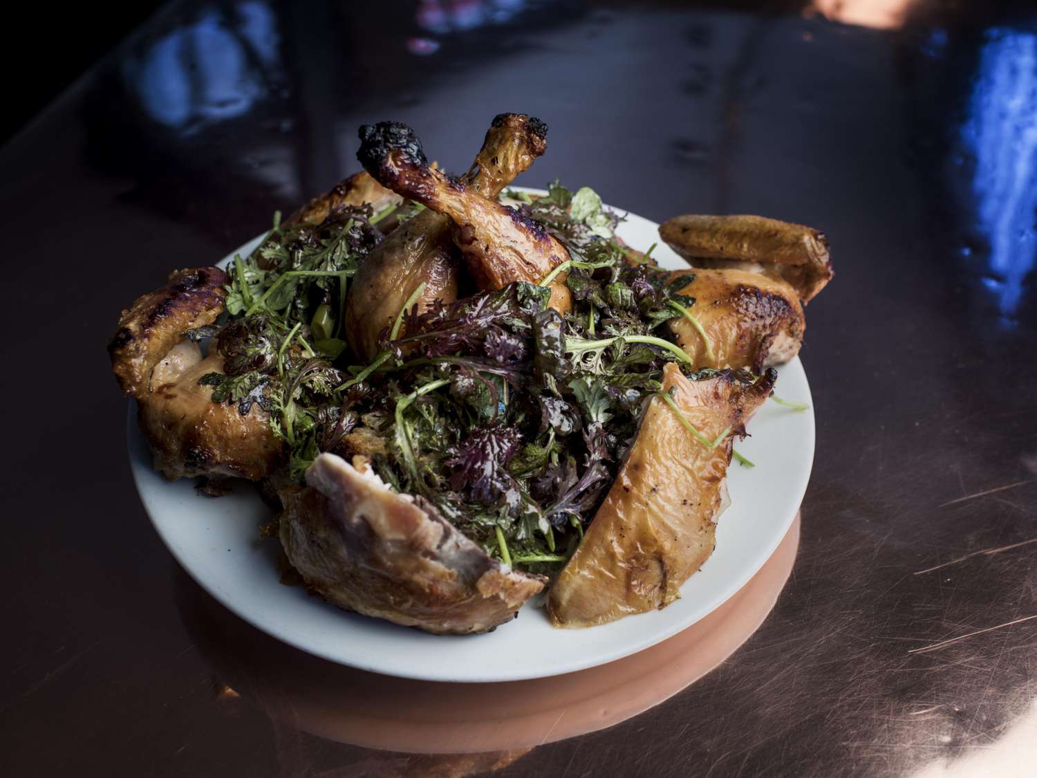 Plate of roasted chicken with greens on a dark surface