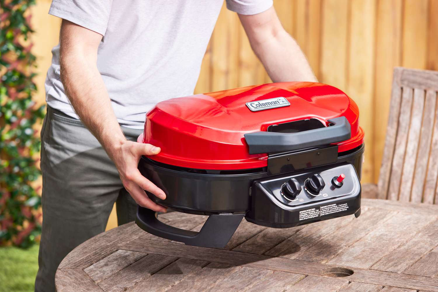 A person sets the Coleman Roadtrip gas grill on a picnic table.