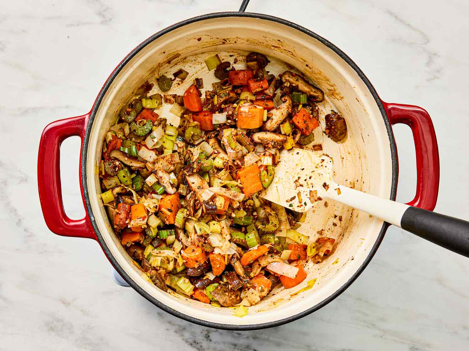 A pot of cooked vegetables including carrots and mushrooms stirred with a spatula