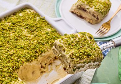 Pistachio tiramisu in a dish a serving being lifted with a spatula revealing layers