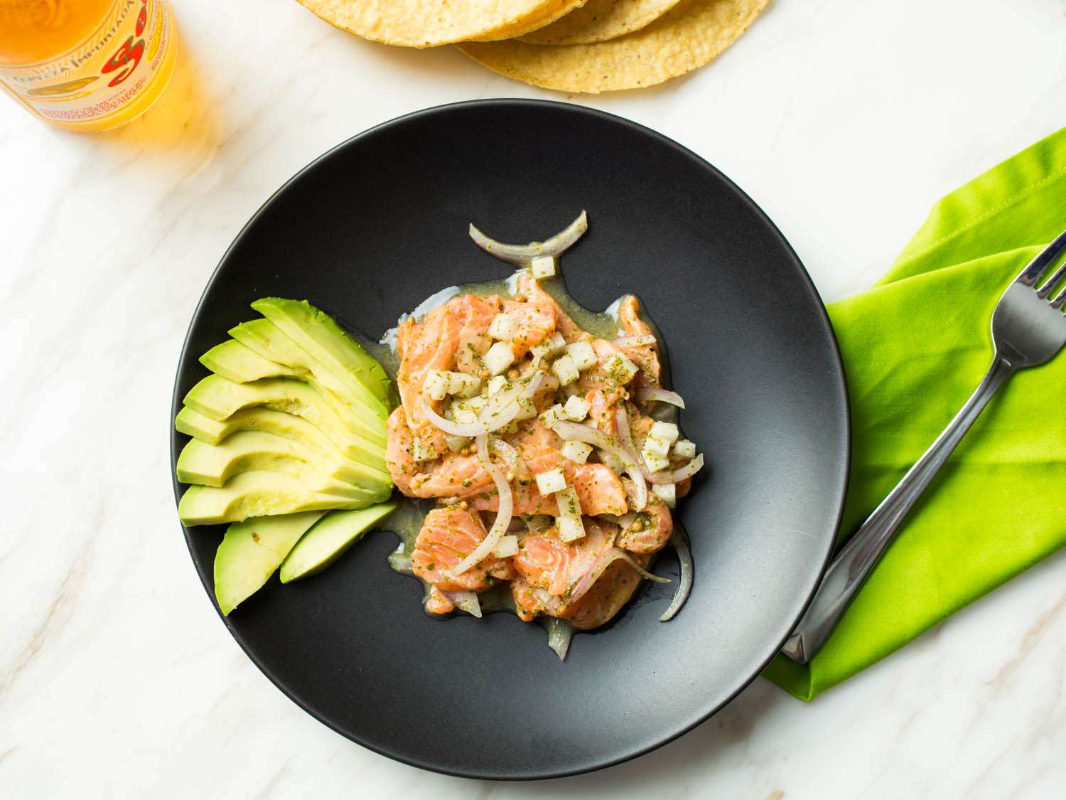 Overhead shot of a bowl of fish aguachile with a side of avocado.