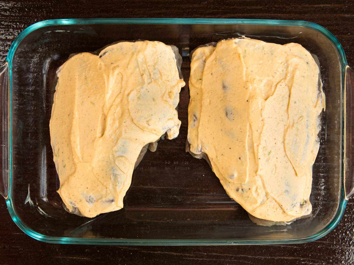 Two bluefish fillets covered in chile-lime aioli in a glass baking dish