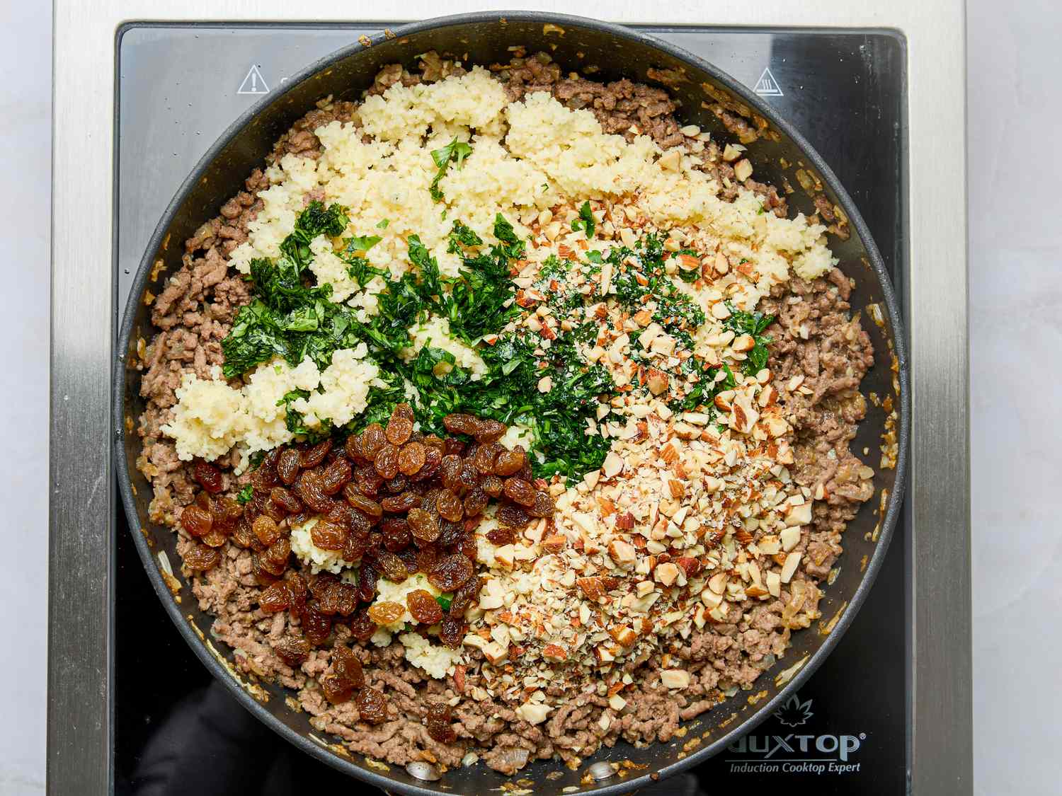 Pan with ground meat raisins chopped herbs nuts and couscous on a cooktop