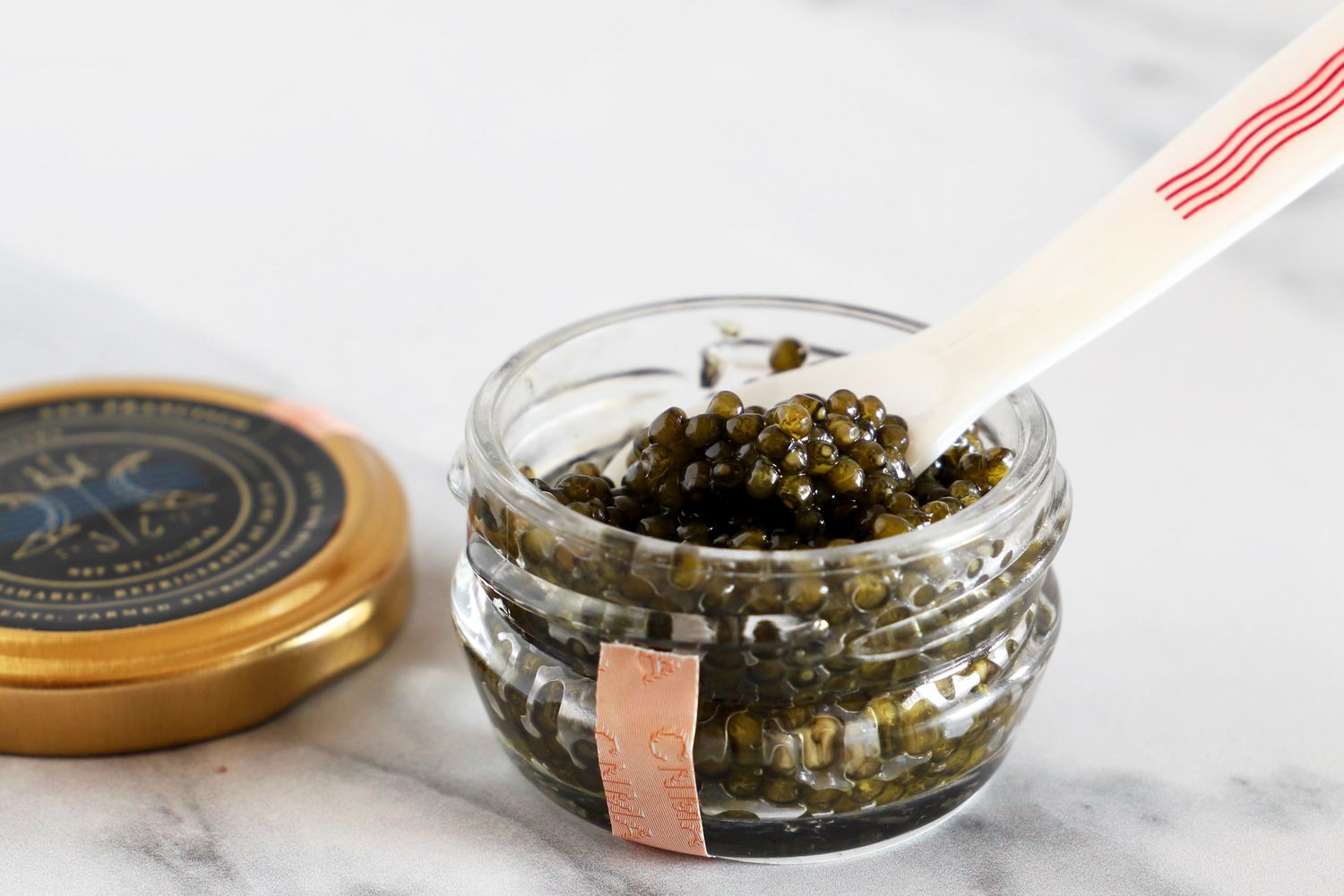 An open jar of Caviar Co osetra caviar with a mother-of-pearl spoon inside