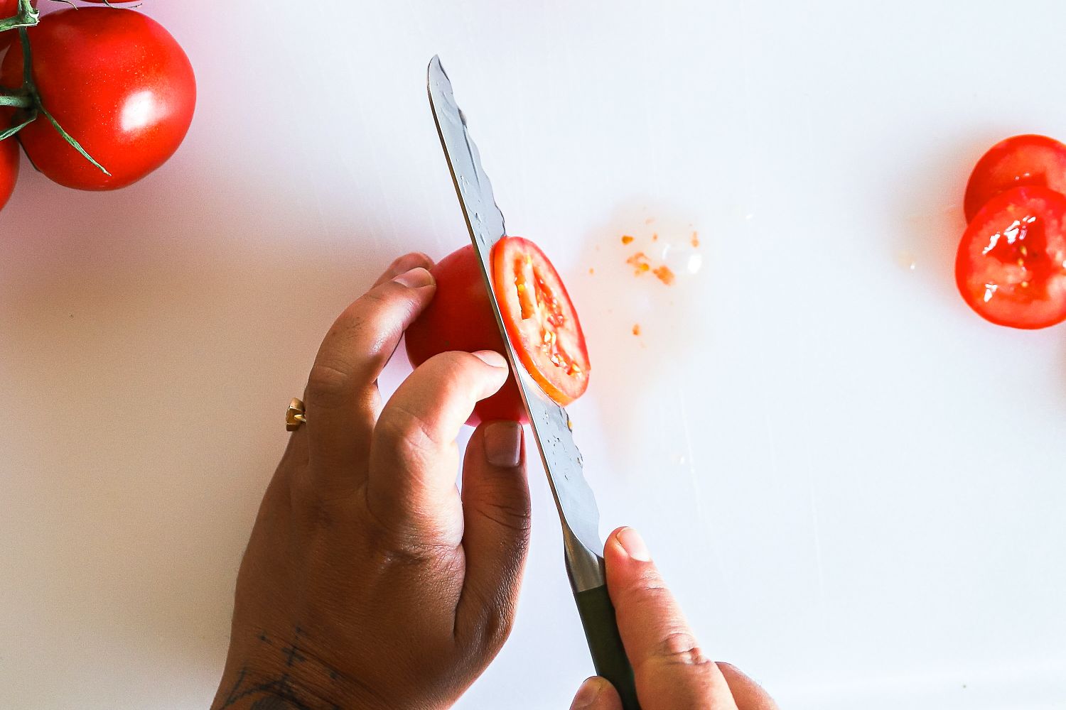 Hands slicing a tomato with a Material knife on a white surface