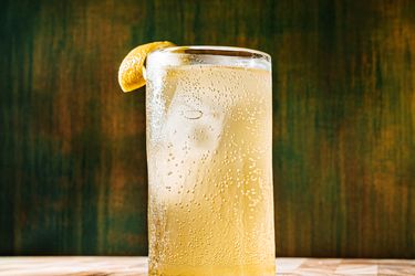 A glass filled with a fizzy lightcolored beverage garnished with a lemon wedge placed on a wooden surface