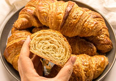 A plate of croissants with a hand holding a halved croissant showing its layers