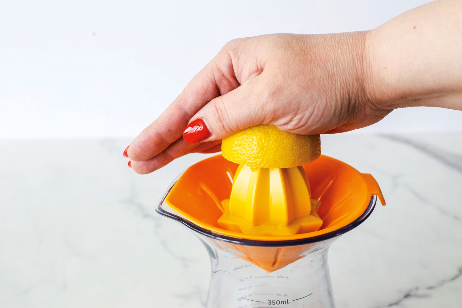 A person using a countertop citrus juicer to juice a half of a lemon.