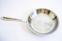 A pan from the All-Clad D3 3-Ply Stainless Steel Cookware Set 10 Piece on a white surface