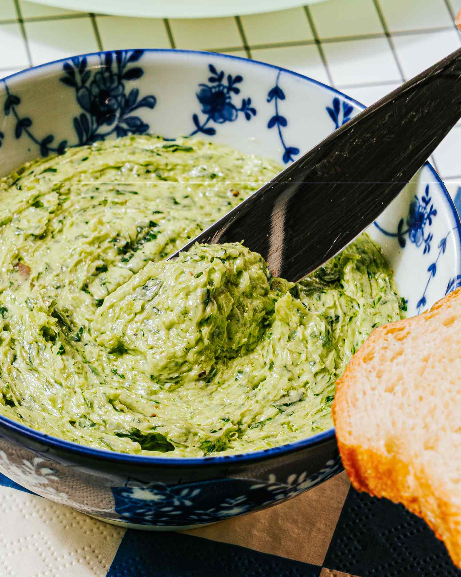 A bowl of escargot butter with a knife and a slice of bread nearby