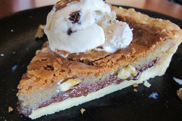 A slice of chocolate chip cookie tart, topped with a scoop of ice cream.