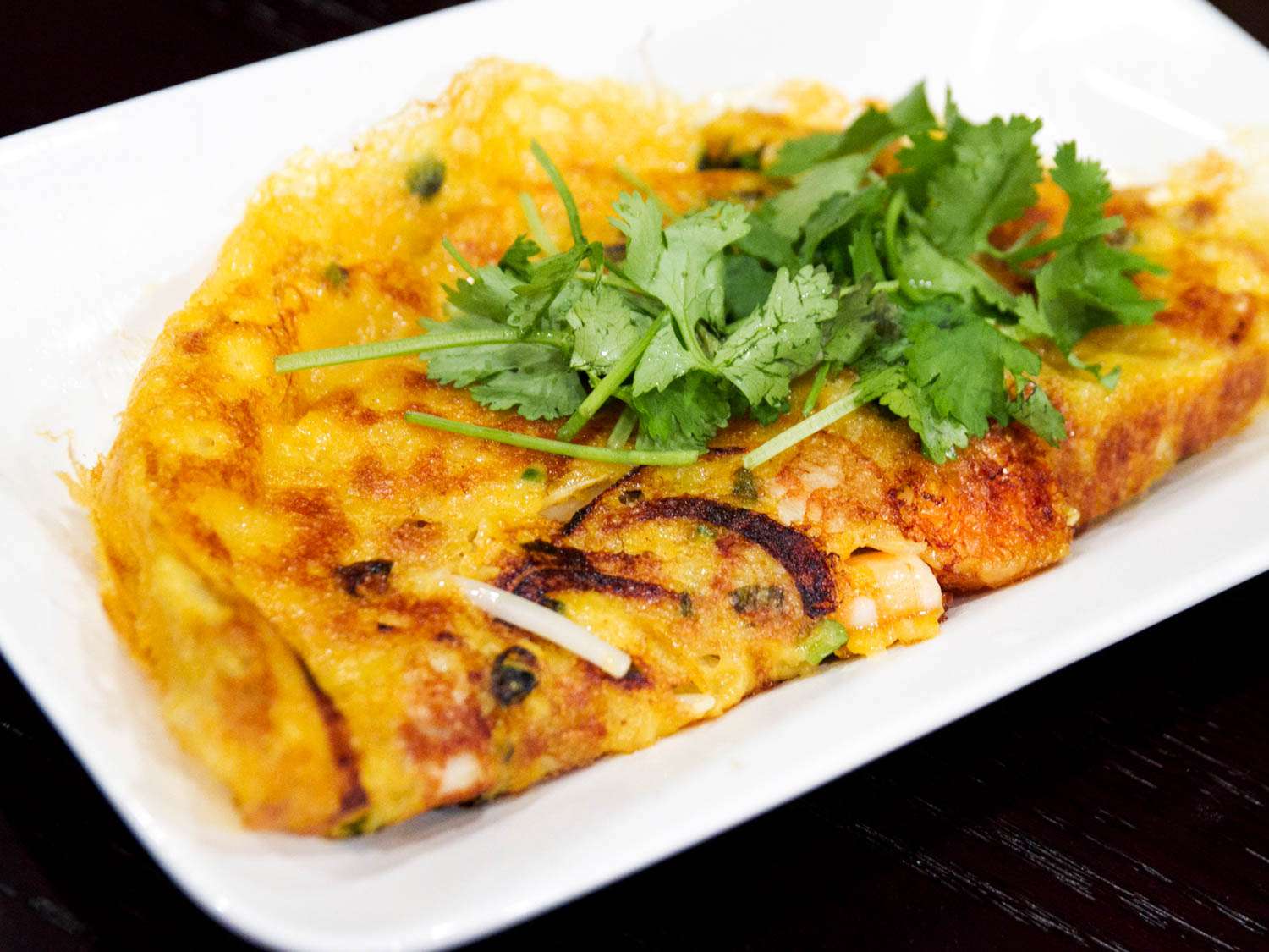 A ban xeo, a Vietnamese rice flour cake on a rectangular plate, topped with fresh cilantro.