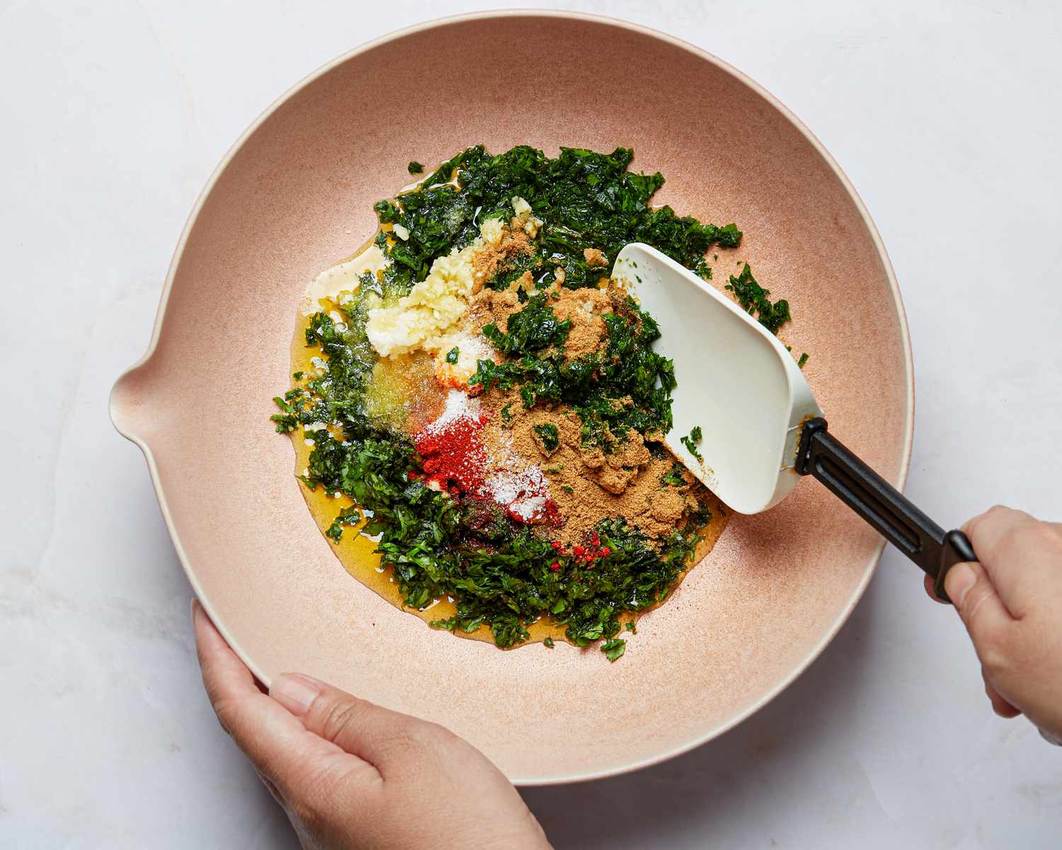 Hands mixing ingredients in a bowl creating a seasoning mixture with herbs and spices using a spatula