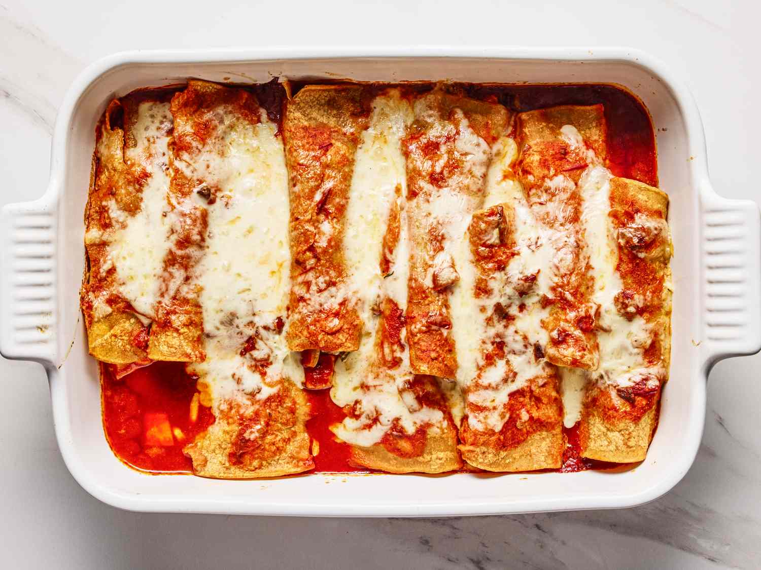 Baked enchiladas topped with melted cheese in a rectangular dish