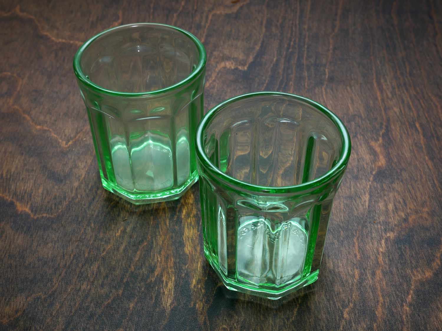 two green glasses on a dark wood surface