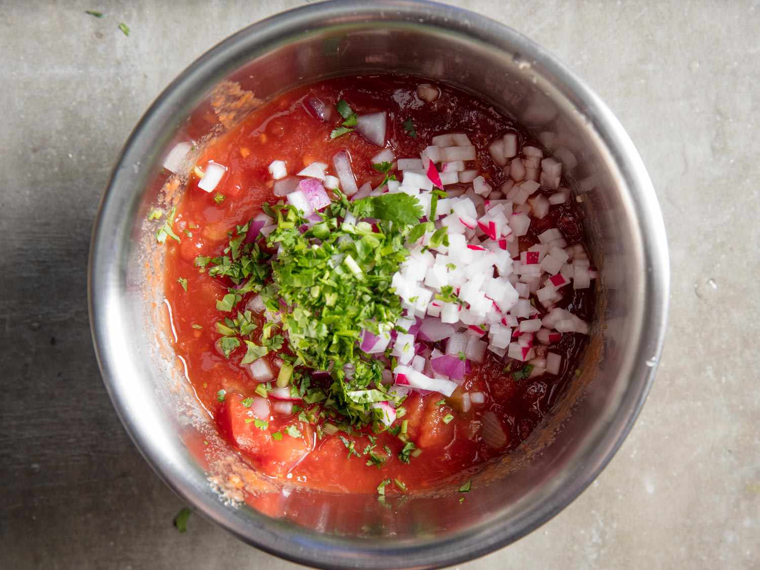 Overhead view of a bowl of salsa with chopped cilantro and diced radish added.