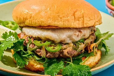 Close-up of a burger with melted cheese, slices of green peppers, cilantro, and a toasted bun on a green plate