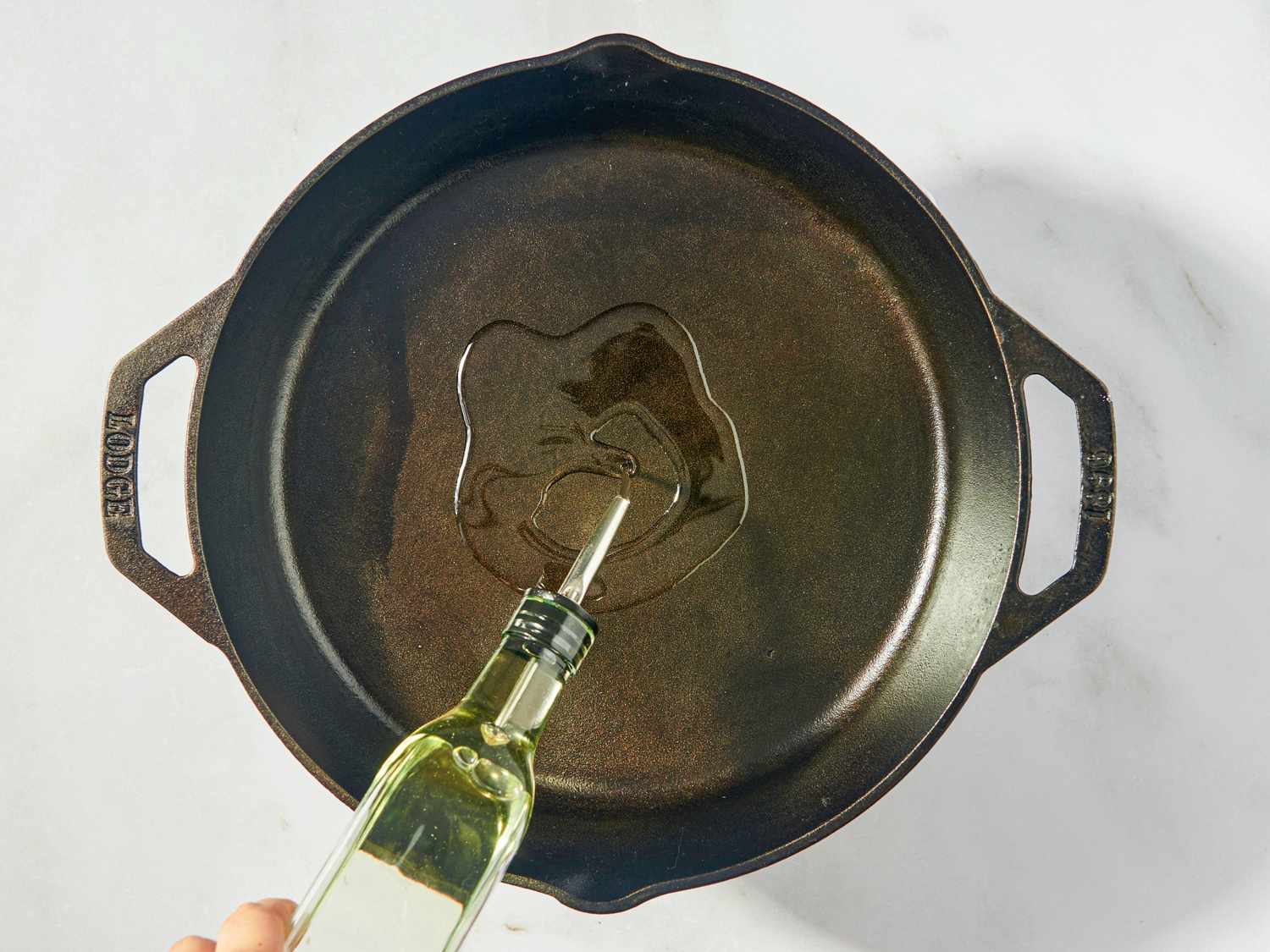 Hand pouring oil into a cast iron skillet