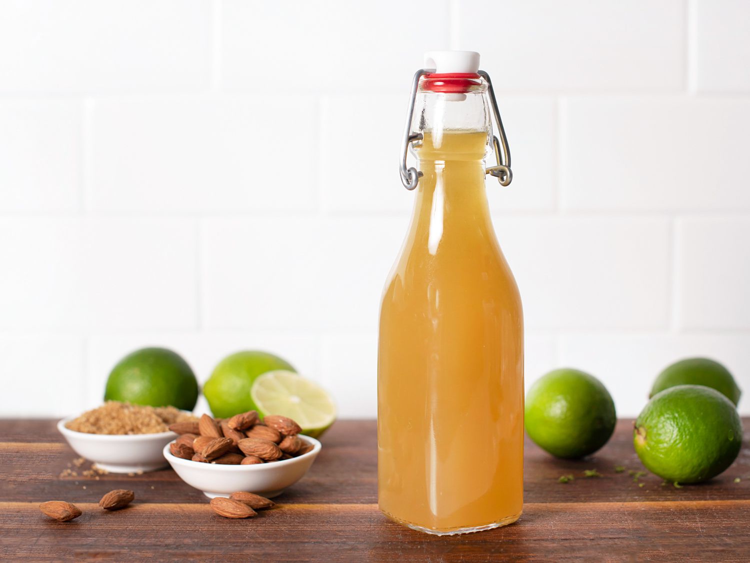 A bottle of homemade Falernum next to plates of almond, sugar, and several limes. 