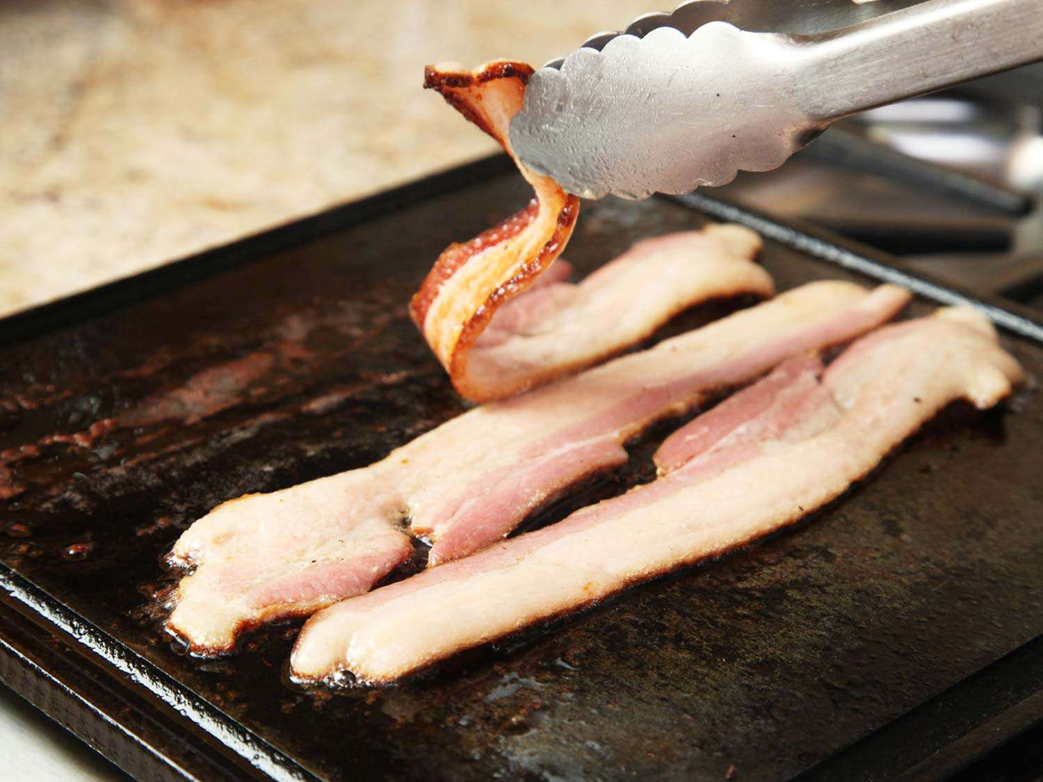 Sous vide bacon being crisped on a griddle.