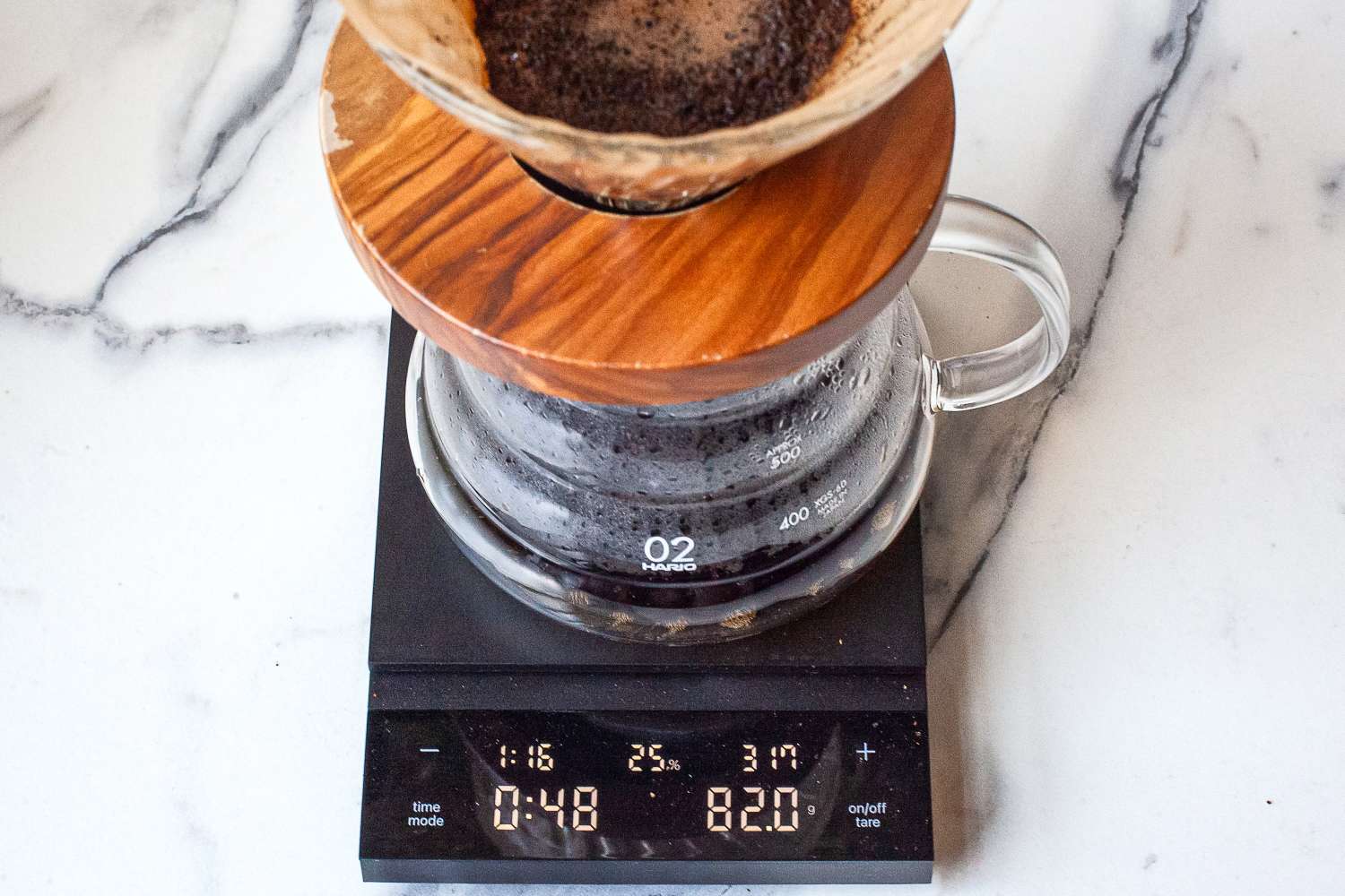 A coffee brewing setup with a wooden dripper on a glass carafe, placed on Hario Polaris Coffee Scale showing readings