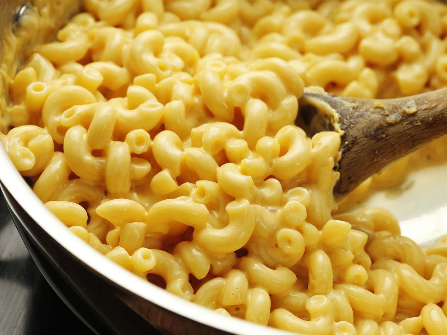 Scooping up 3-ingredient macaroni and cheese with a wooden spoon.