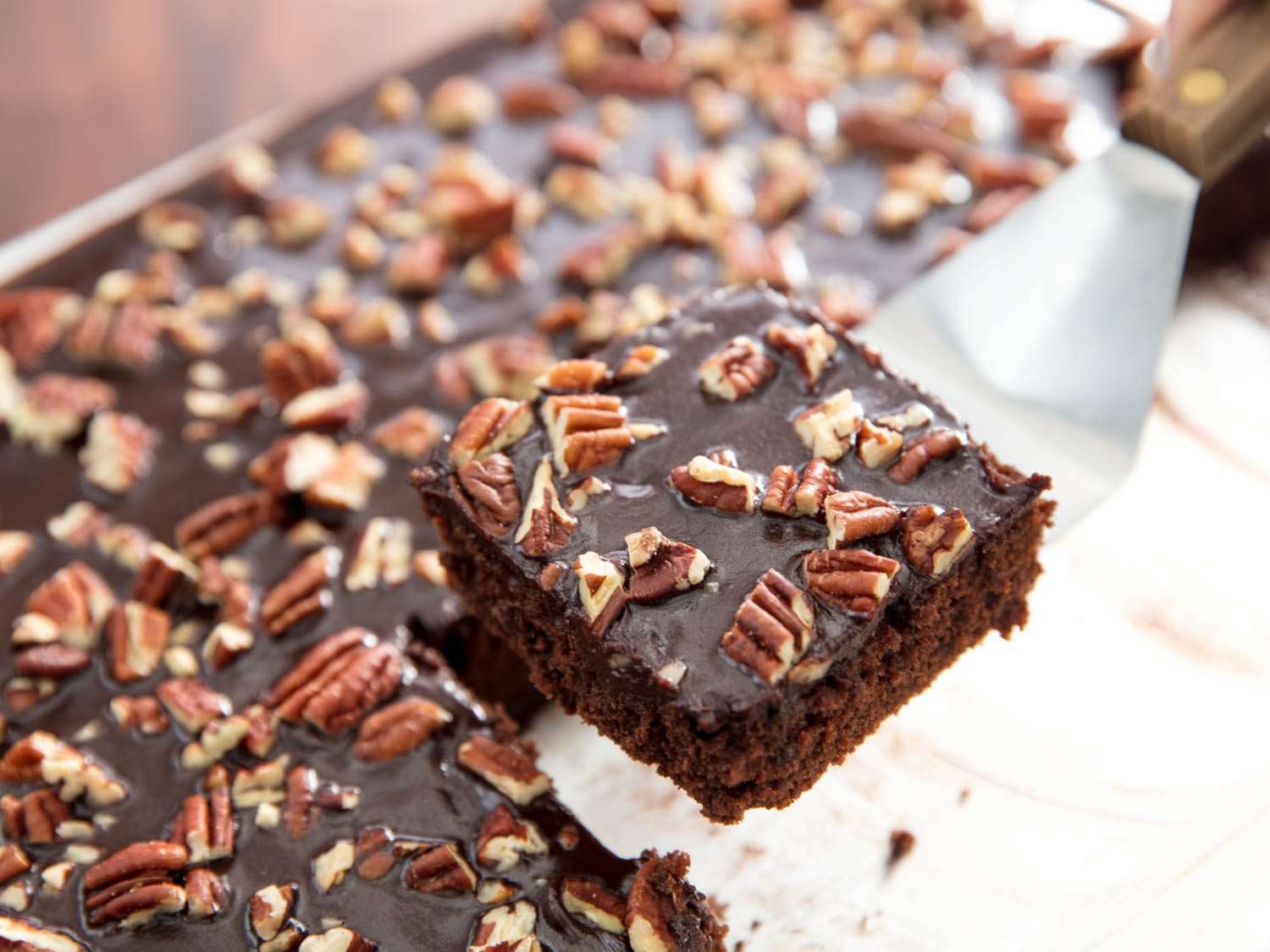 An offset spatula lifting a square of Texas sheet cake from the finished cake.