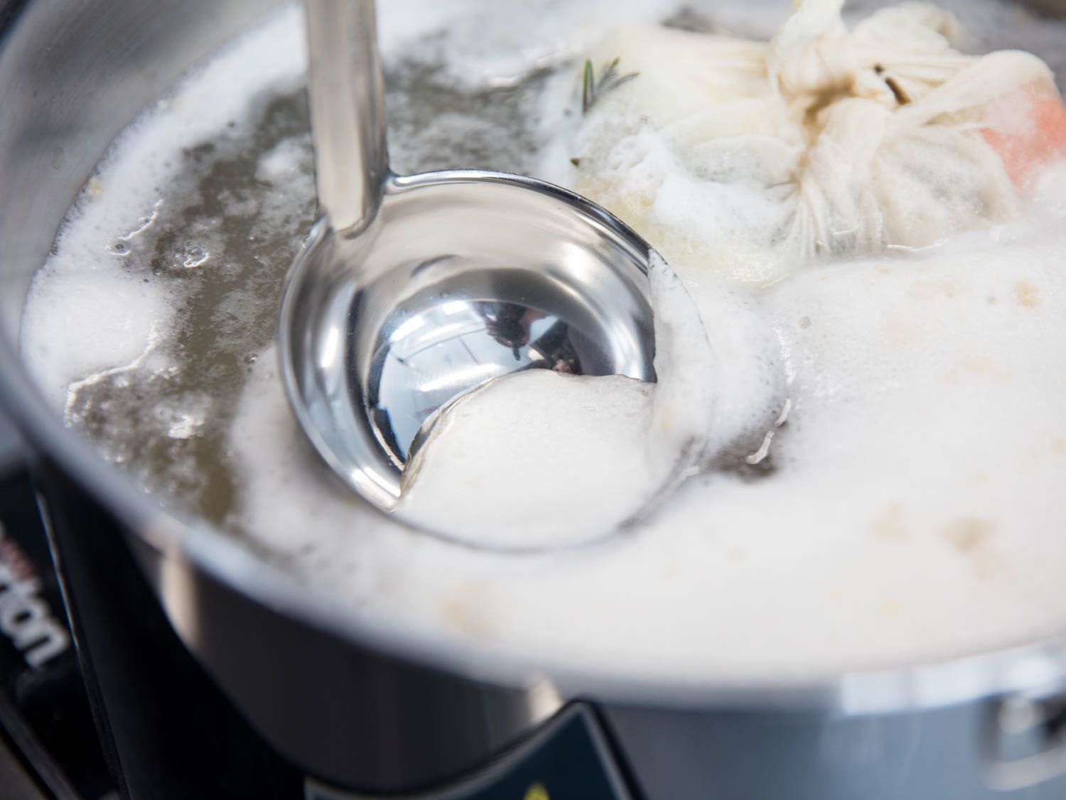 Using a ladle to scoop up the white foam in a pot of simmering beans.
