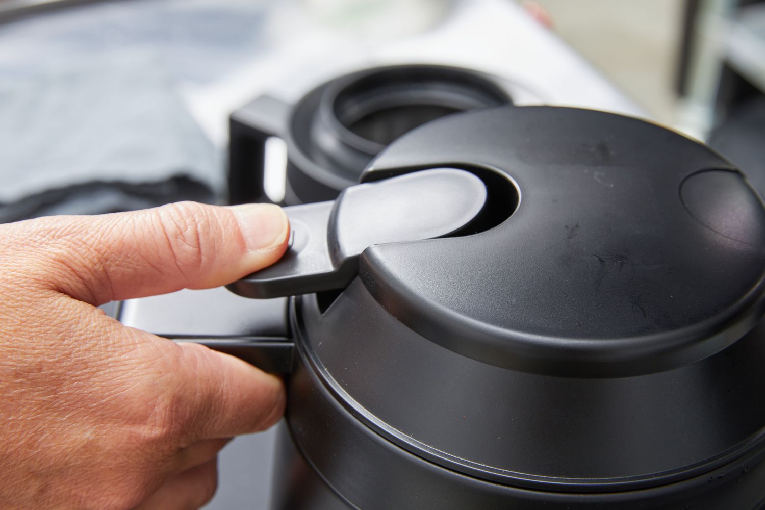 Close-up of a thumb pushing on the spout opener for the Ratio Six Coffee Maker's carafe.