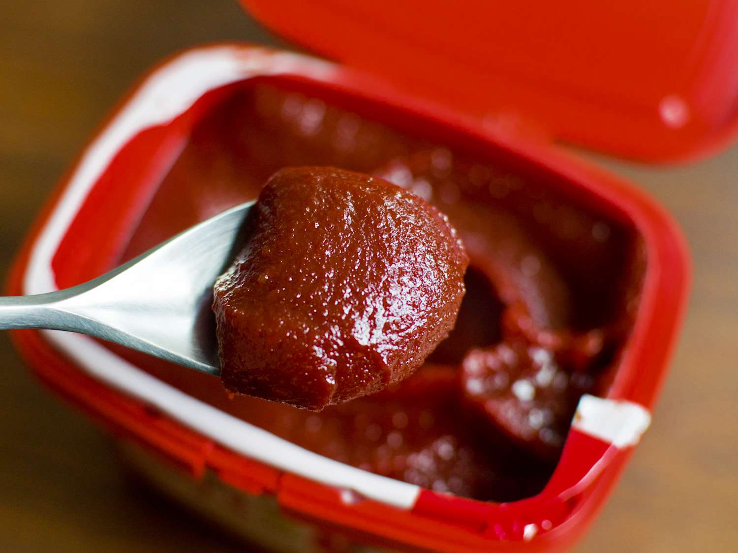 A spoonful of gochujang being taken from a tub.