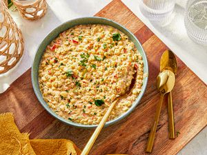 A bowl of creamy corn garnished with herbs on a wooden surface with golden utensils alongside
