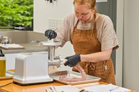 Person making sausage using Weston #12 Electric Meat Grinder & Sausage Stuffer while pushing meat from tray